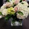 Low arrangement of white hydrangeas and blush roses in a clear glass cube vase