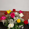 Mixed red, pink, yellow, and white roses with baby's breath in a clear glass vase on a dark countertop
