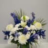 Tall arrangement of white lilies, roses, mums, and blue flowers in a green glass vase