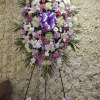 Tall standing spray of white, lavender, and pink flowers with a large lavender bow on an easel.