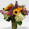 Tall mixed bouquet with sunflowers, roses, lilies, hydrangeas and purple flowers in a clear glass vase