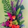 Tall tropical bouquet with orange roses, magenta blooms, and purple accents