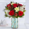 Red roses and white carnations in a blue glass vase with pinecones
