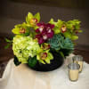 This arrangement is in a black ceramic vase with orchids, hydrangeas, and
