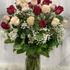 Tall arrangement of red and pale pink roses with white baby's breath in a clear glass vase