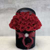 Round black hatbox filled with red roses, tied with a red bow and jeweled brooch.