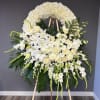 Large white funeral wreath on an easel with lilies and roses