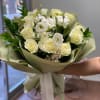 Bouquet of white and pale yellow roses with white blooms wrapped in sage paper