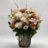 Bouquet of blush and peach roses with white accent flowers in a tall vase