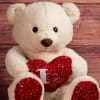 White teddy bear holding a red heart pillow
