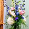 Mixed bouquet in a clear glass vase with pink roses, white lilies, and blue flowers