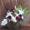 Mixed bouquet with white lilies, orchids, and burgundy blooms in a glass vase