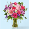 Bouquet of pink roses, lilies, and purple flowers in a clear glass vase