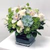 White roses and orchids arranged with a blue-green succulent in a square glass vase.