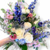 Handheld bouquet of white, pink, and blue flowers with long stems