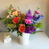 Colorful mixed bouquet in a white vase with pink, orange, purple, and blue flowers