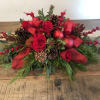 Red roses with pinecones, berries, and ribbon in a low holiday arrangement