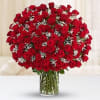 Large bouquet of red roses with white filler flowers arranged in a clear glass vase