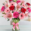 Pink and red bouquet of roses, lilies, and gerbera daisies in a glass vase