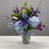 Mixed bouquet of blue hydrangeas, purple lilies, and green accents in a glass vase
