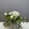 White roses and lilies in a gray container with trailing greenery