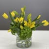 Yellow tulips and lilies arranged in a clear glass vase with green hydrangea