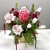 Mixed bouquet with pink protea, pale roses, and white tulips in a gold vase