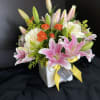 Pink lilies and white roses in a white vase with a yellow ribbon