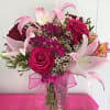 Pink roses and lilies arranged in a glass vase with a pink ribbon