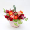 Mixed bouquet of red, pink, and orange flowers in a pale pink vase