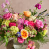 Mixed bouquet of pink, peach, and purple flowers in a clear glass vase