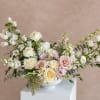 Soft pastel bouquet of roses, ranunculus, and white blooms in a white bowl vase
