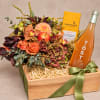 Flower gift box with orange blooms, chocolate, and a rosé bottle