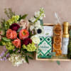 Mixed flower bouquet beside a gift tray with snacks and olive oil