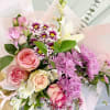 Bouquet of pink roses, purple daisies, and white lilies in pale wrapping