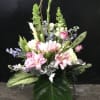 Tall bouquet of pink lilies, white callas, and blue flowers with large tropical leaves