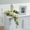 White rose floral tribute draped over a white urn