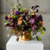 Mixed bouquet of purple, peach, and burgundy flowers in a gold vase