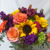 Colorful bouquet with sunflowers, peach roses, and purple blooms in a glass vase