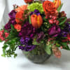 Mixed bouquet of orange, purple, and lime flowers in a glass vase
