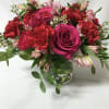 Bouquet of pink roses, red carnations, and pale alstroemeria in a glass vase