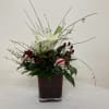 White lilies and red roses in a square glass vase with holiday accents