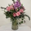 Pink roses and purple flowers arranged in a clear glass vase