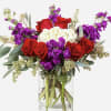 Bouquet of red roses, purple flowers, and white blooms in a glass vase