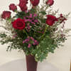 Red roses arranged in a tall burgundy vase with pink filler flowers