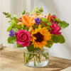 Bright mixed bouquet with sunflowers, roses, lilies, and a glass vase