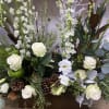 White roses and mixed flowers arranged in a wooden box with pinecones