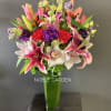 Tall bouquet of pink lilies, roses, and orchids in a glass vase