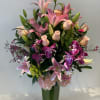 Pink lilies, roses, and orchids arranged in a tall glass vase