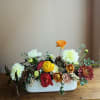 Mixed flower arrangement in a white rectangular vase with orange, red, yellow, and white blooms